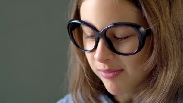 A girl in big black glasses looks down. Close up view. — Stock video