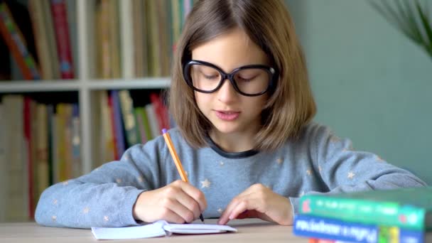 El niño escribe una solución al problema en un cuaderno. Una mirada emocional frente a ti. Vista de cerca . — Vídeos de Stock