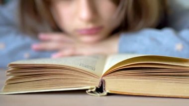 In the foreground is a book. A girl is reading a book. Close up view.