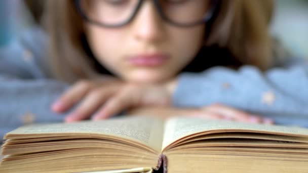 큰 검은 안경을 쓴 소녀가 책을 읽고 있습니다. 앞쪽에는 책 이 있습니다. 가까이 서 본 모습. — 비디오