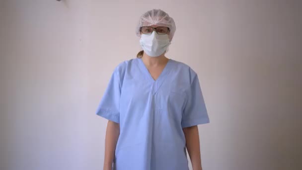 Female doctor in the protective mask and hat looks directly at the camera with white blank in hands. — Stock Video
