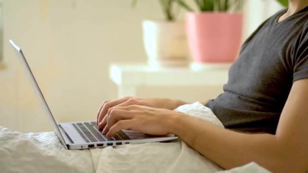 Un uomo lavora in camera da letto con un portatile a casa. Concetto di lavoro a distanza . — Video Stock
