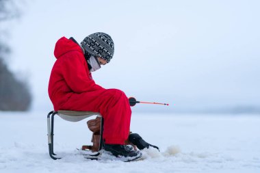 Gölde kışın balık tutan kırmızı tulumlu küçük bir çocuk. Oltaya dikkatlice bak. Ufuk gökyüzü ile birleşir. Her yer beyaz kar..