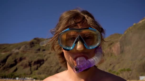 Mladý muž s šnorchlem a brýlemi pro potápění, stojí na pobřeží. — Stock video
