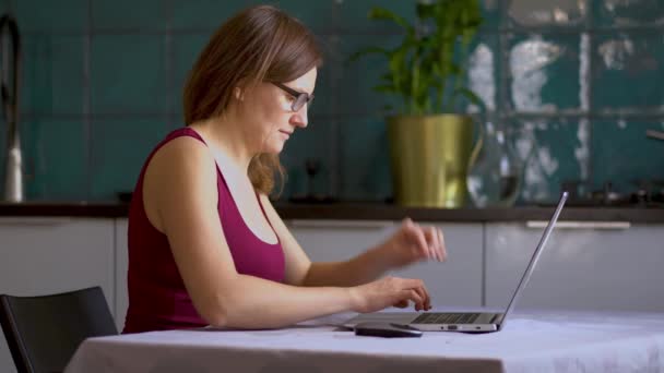 En kvinna jobbar i köket på en laptop. Fjärrarbete i hemmet under karantänsperioden för coronavirus Covid 19. — Stockvideo