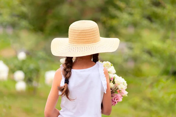 Una chica con coletas sostiene en sus manos un ramo de peonías blancas y rosadas. Vista trasera . — Foto de Stock