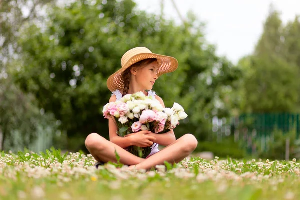 Букет з рожевих і білих півоній в руках дівчини, що сидить на квітучому лузі . — стокове фото