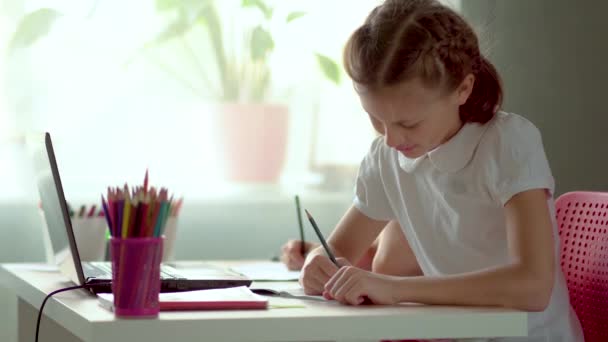 Симпатичный ребенок использует ноутбук для обучения, онлайн-обучения, домашнего обучения. Девочка имеет домашнее задание на дистанционном обучении . — стоковое видео