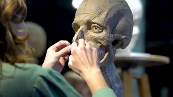 Vrouw beeldhouwer aan het werk op een sculptuur van een menselijk hoofd. — Stockvideo