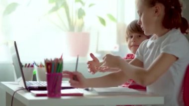 Evde çocuklar için uzaktan öğrenme. Bir abla erkek kardeşine dizüstü bilgisayarda ödevlerinde yardım eder..