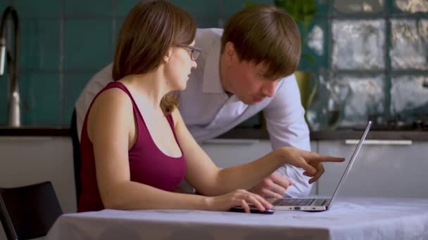 Un homme et une femme travaillent dans la cuisine sur un ordinateur portable. Travail à distance à domicile pendant la période de quarantaine du coronavirus Covid 19 . — Video