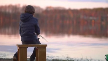 Küçük çocuk gün batımında gölde balık tutuyor.