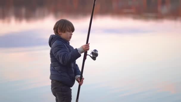 Liten pojke fiskar vid solnedgången på sjön — Stockvideo