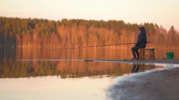 Den lille gutten fisker ved solnedgang på sjøen. – stockvideo