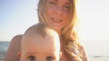 Mutlu aile, anne ve bebek gün batımında deniz sahilinde oturuyor. Yaz tatilinde çocuklu ebeveyn