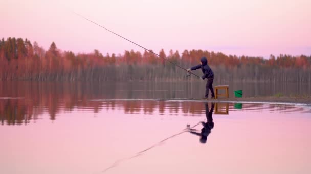 Мальчик рыбачит на рассвете на озере — стоковое видео