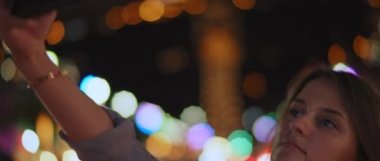 Caddenin ortasında selfie çeken ve gülümseyen genç bir kadının gece lambaları. Sığ dof, gerçek zamanlı, Bmpcc 4k