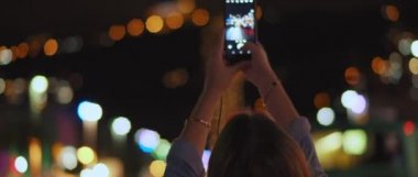 Caddenin ortasındaki bir gece şehrinin fotoğrafını çeken genç bir kadın, arka planda da bokeh ışıkları. Sığ dof, gerçek zamanlı, Bmpcc 4k