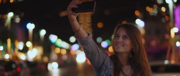 通りの真ん中で自撮りをしている若い女性と笑顔 夜の街のボケのライト 浅いDof リアルタイム Bmpcc — ストック動画