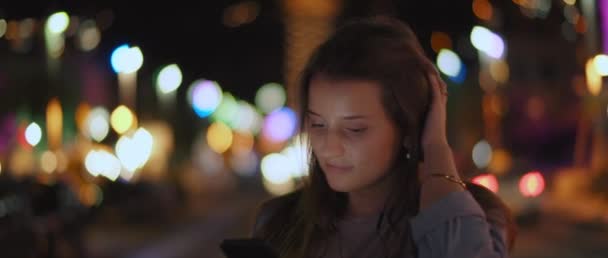 通りの真ん中の携帯電話で音楽を聞いている若い女性が 背景にボケの光を当てている 浅いDof リアルタイム Bmpcc — ストック動画