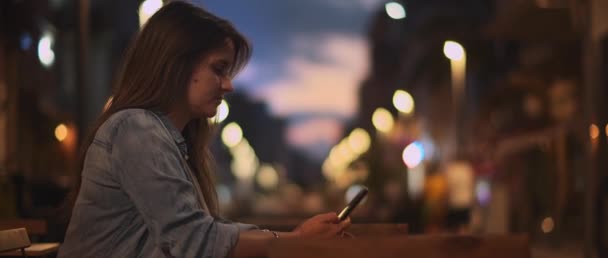 Молодая Женщина Джинсовой Рубашке Сидящая Кафе Фотографирует Ночной Город Боке — стоковое видео