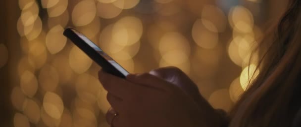Закройте Руки Молодой Женщины Прокручивающей Соцсетях Свой Телефон Боке Огнями — стоковое видео