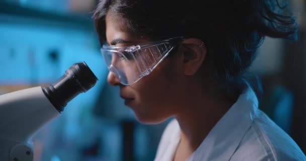 Forscherin Schaut Ins Mikroskop Trägt Schutzbrille Blaue Beleuchtung Dunklem Laborraum — Stockvideo