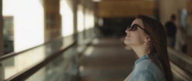 Yürüyen bir geçitte, güneş gözlüklü ve yüzünde bir ışık olan bir kadın etrafına bakıyor. Yavaş çekim sinematik çekim. Bmpcc 4k