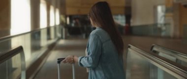 Uzun saçlı, kot gömlekli, havaalanının terminalinde bavuluyla yürüyen bir geçitten inen bir kadın. Yavaş çekim sinematik çekim. Bmpcc 4k