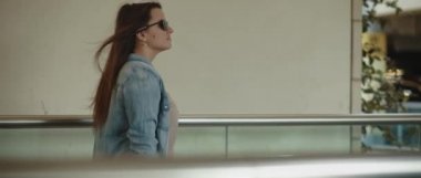 Uzun saçlı, güneş gözlüklü, yürüyen bir yolda yürüyen bir kadın. Yavaş çekim, takip çekimi. Cinemati görüntüleri, Bmpcc 4k