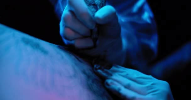 白い手袋のタトゥーアーティストは 人の肌に入れ墨を描く スローモーション 青のスタジオ照明 フィールドの浅い深さ Bmpcc — ストック動画