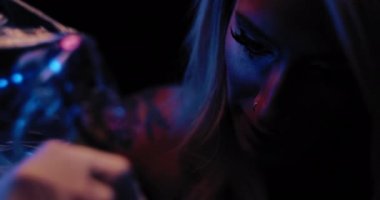 Stüdyosunda dövme yaptıran genç bir kadın dövme ustasının fotoğrafını çek. Yavaş çekim, mavi stüdyo ışıkları, sığ alan derinliği. BMPCC 4K