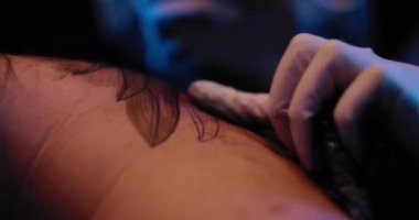 Dövme sanatçısının elinin, birinin sırtına dövme çizimi yaparken yakın plan. Yavaş çekim, mavi stüdyo ışıkları, sığ alan derinliği. BMPCC 4K