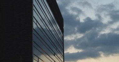 Gün batımında gökdelen binası. Mavi gökyüzü ve bulutların cam yansıması. Kuşlar uçuşuyor. Düşük açı, el kamerası, yavaş çekim. Bmpcc 4k