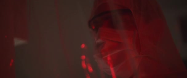 マスクとメガネで保護スーツの男の閉じると 周りを見回す 健康と安全の生活 ウイルス保護 パンデミックの概念 背景に赤い光 スローモーション Bmpcc — ストック動画