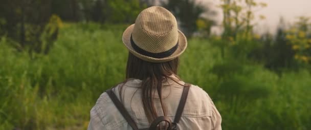 夕阳西下 一个年轻姑娘背着背包 戴着一顶帽子 在绿地里被拍了下来 缓慢的运动 Shallow Dof 生活方式的概念 Bmpcc — 图库视频影像