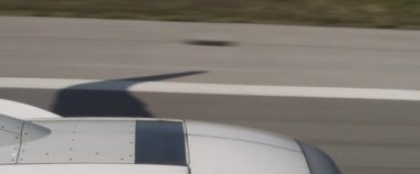 Uçak, kanadın gölgesiyle pistten kalkıyor, bir uçağın içinden görünüyor. Uçak pistte çok hızlı hareket ediyor. Macera, seyahat, seyahat konsepti. BMPCC 4K
