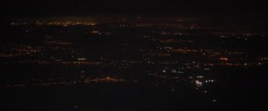 Geceleri uçak penceresinden şehrin havadan görünüşü. Gece vakti yollar ve binalar üzerinde uçan bir uçak. Macera, seyahat, seyahat konsepti. Yavaş Hareket, BMPCC 4K. 