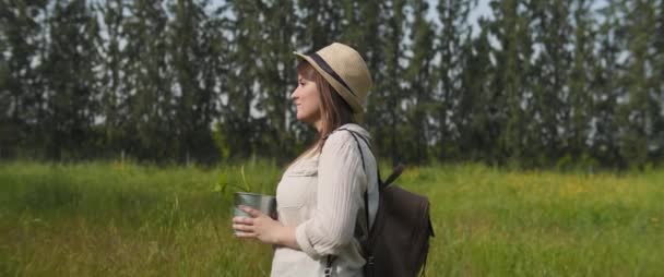 拿着帽子 背包和旧胶卷相机的年轻女子背着盆栽走过绿地 地球日 新的生命概念 中型射击 慢动作 Bmpcc — 图库视频影像