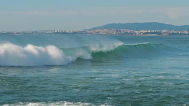İnsanlar Portekiz 'in Lizbon kıyısında sörf yaparken büyük bir okyanus dalgası kıyıya doğru akıyor. Ağır çekim, BMPCC 4K.