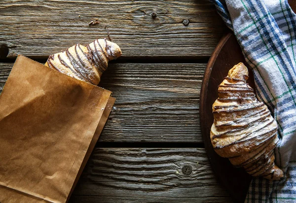 Färska croissanter i papperspåse på trä bakgrund — Stockfoto