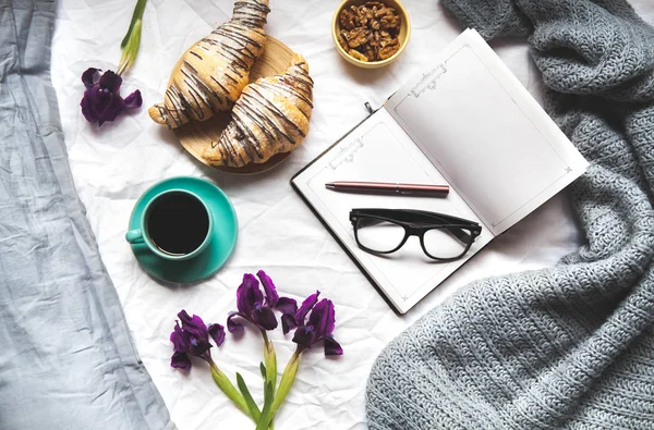 Pequeno-almoço na cama. Bom dia, croissant, café, flores e um caderno com caneta. Planeamento — Fotografia de Stock