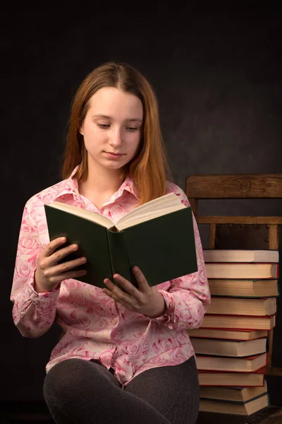 附近一摞书的十几岁女孩阅读书的肖像. — 图库照片
