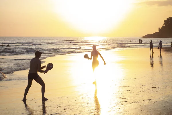 Az emberek a parton játszanak napnyugtakor. Stock Kép