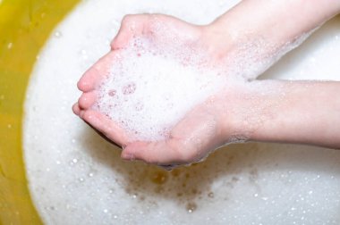 Çocuk ellerini sarı bir su havzasında sabunla yıkıyor. Virüslerden el dezenfeksiyonu