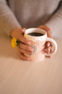 Elinde bir kupa sade kahve tutan çiçek yüzüğüyle kadın elleri.