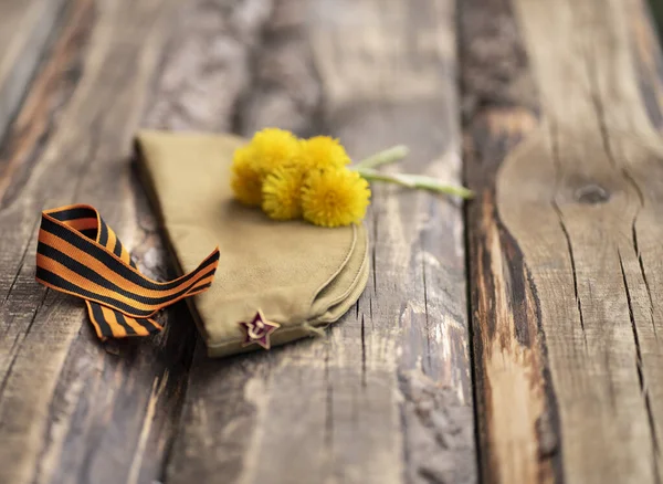 9 Mayıs zafer günü geçmişi. Askeri şapka, sarı çiçekler, St. George kurdelesi. Ahşap arkaplan.