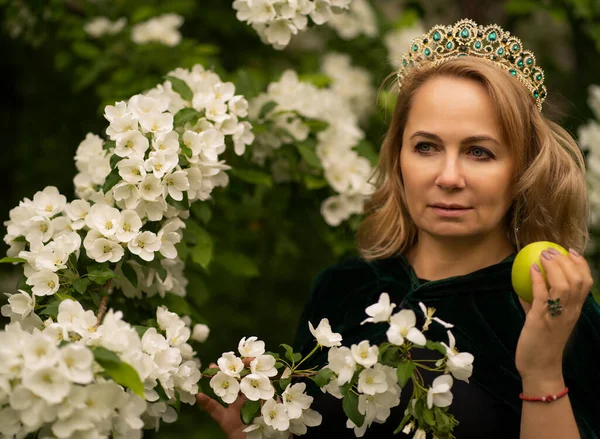 Genç ve güzel bir kadın bir elma ağacının beyaz çiçeklerinde duruyor ve başka tarafa bakıyor. Yeşil taşlı bir taç ve kadife yeşil bir başlık takıyor ve elinde bir elma tutuyor.