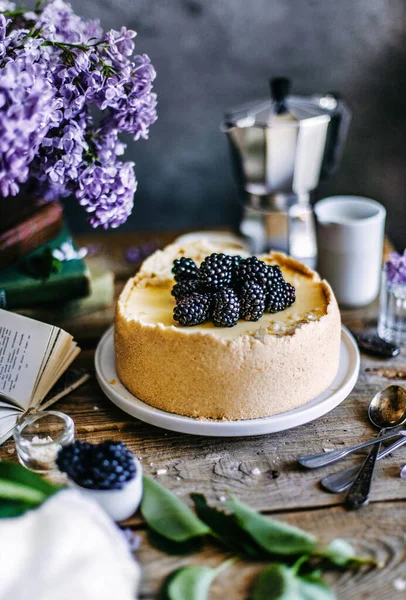 New York Cheesecake with blackberry berries on a wooden table with lilac bouquet