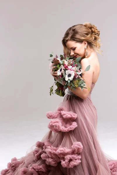 Mulher bonita em um vestido rosa posando com um buquê . — Fotografia de Stock